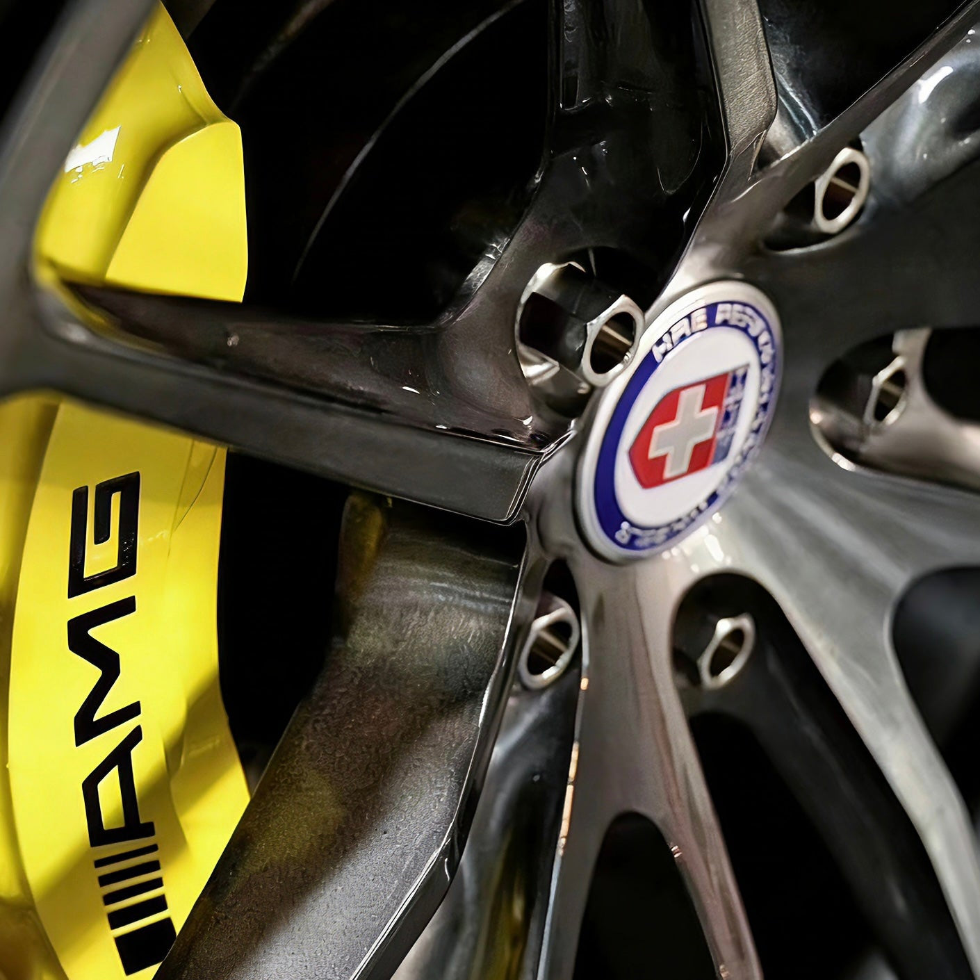 Close-up of a car wheel with a visible HRE aftermarket rims logo on a yellow amg brake and titanium wheel lug bolts
