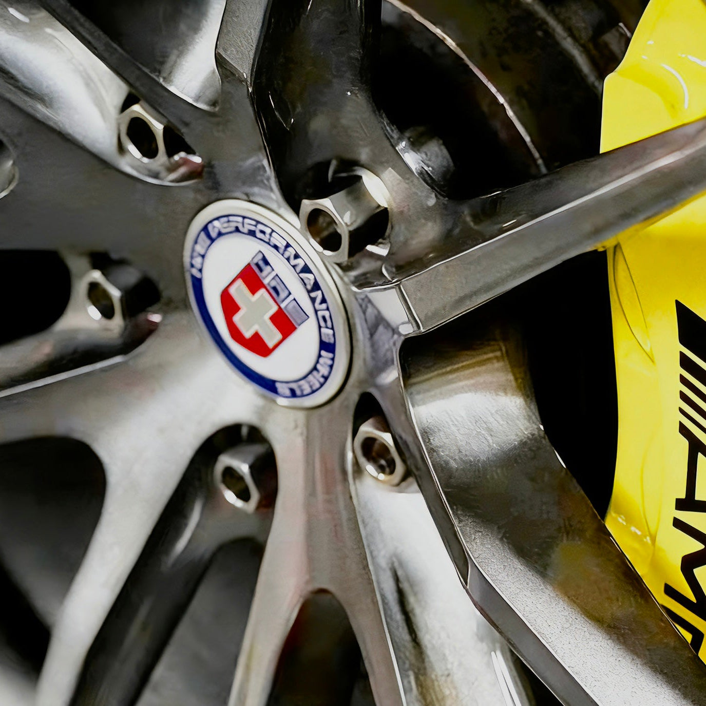 Close-up of a car wheel with a visible HRE aftermarket rims logo on a yellow amg brake and titanium wheel lug bolts
